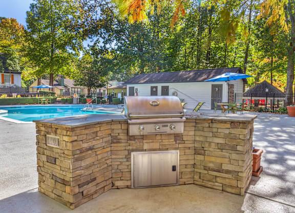 A stone wall with a grill on top and a pool in the background.