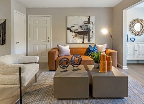 A living room with a white chair, a brown couch, and a large painting on the wall.
