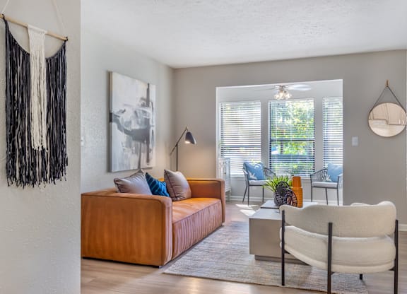 A living room with a brown couch, a white chair, and a hanging decoration on the wall.