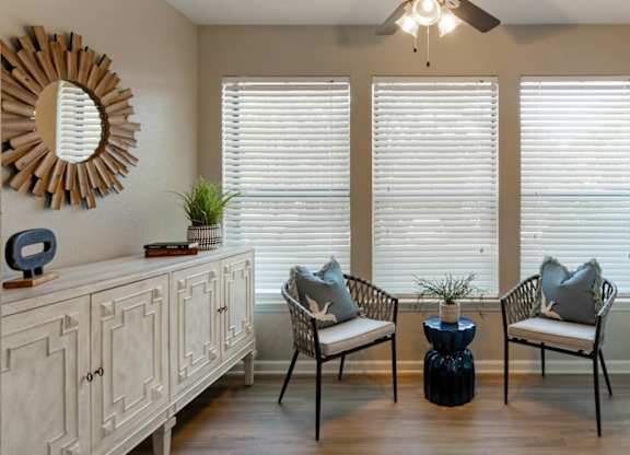 A living room with a wooden floor, a white cabinet, a mirror, a ceiling fan, and a window with blinds.