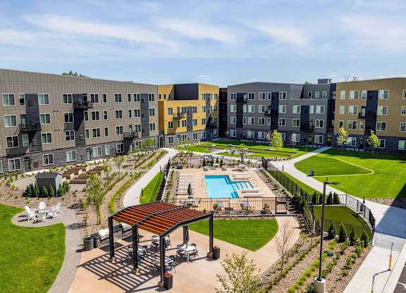 A large outdoor swimming pool is surrounded by a grassy area and a wooden pavilion.