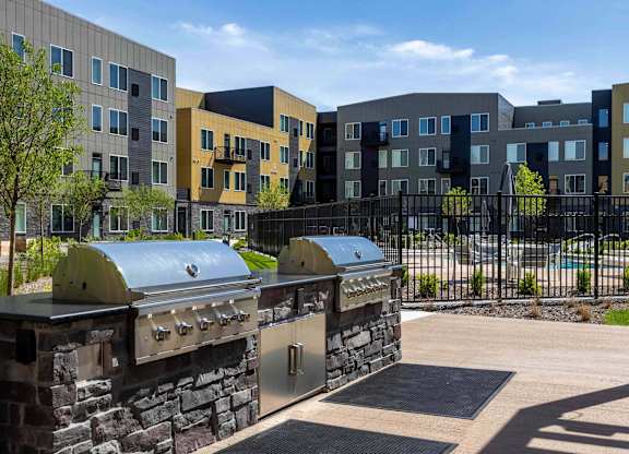 A modern outdoor kitchen area with grills and a stone wall in front of apartment buildings.