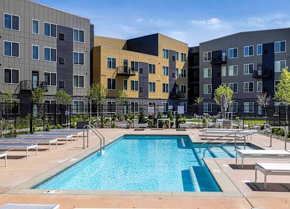 A swimming pool surrounded by lounge chairs in front of apartment buildings.