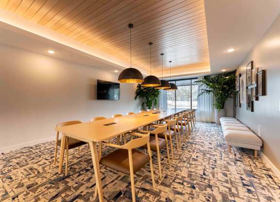 A long wooden table is surrounded by chairs in a room with a patterned carpet.