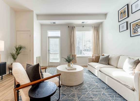 A living room with a white couch, a wooden chair, and a small table with a vase on it.