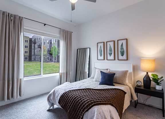 A bedroom with a large bed and a window overlooking a green area.