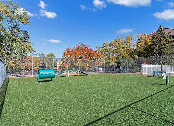 A green artificial turf field with a blue water tank and a white fence.
