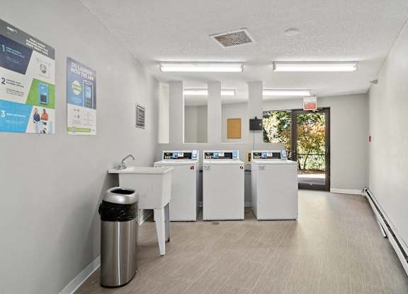 A clean, well-lit room with a white table, a trash can, and a wall with posters and a window.