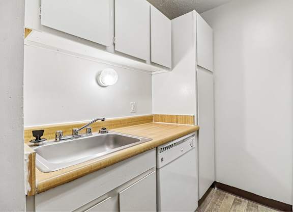A kitchen with a white fridge, sink and cabinets.
