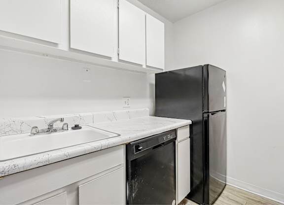 A black refrigerator is in a kitchen with white cabinets.