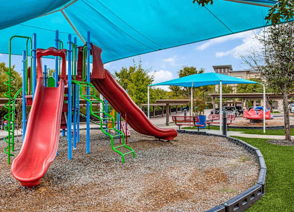 A playground with a red slide and a blue canopy at Twin Creeks Crossing
