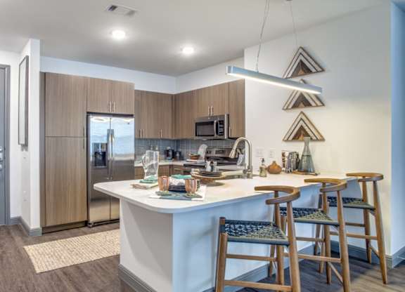 Open kitchen with breakfast bar and wood-style cabinetry at Twin Creeks Crossing, Allen apartments
