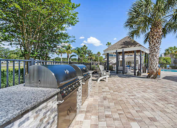 A gazebo is surrounded by a brick walkway and palm trees.