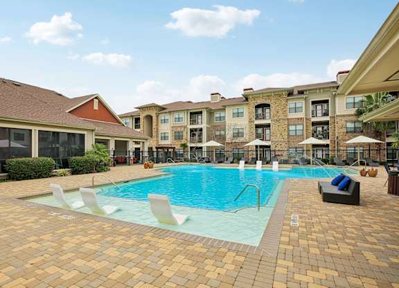A large swimming pool surrounded by a brick patio and lounge chairs.