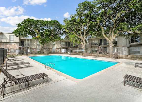 A swimming pool surrounded by trees and lounge chairs in a residential area.