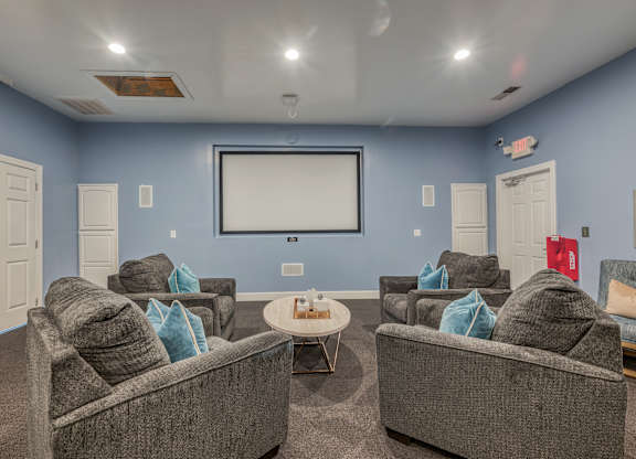 A living room with grey couches and a white screen.