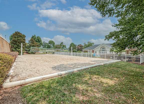 A large, empty sand pit sits in the middle of a grassy area.