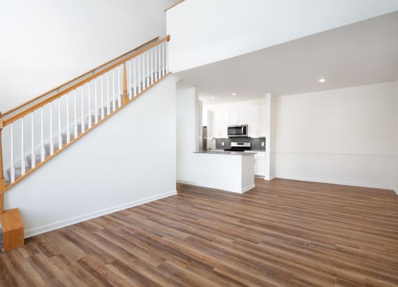 View of vacant living room with stairs up to loft and kitchen in background