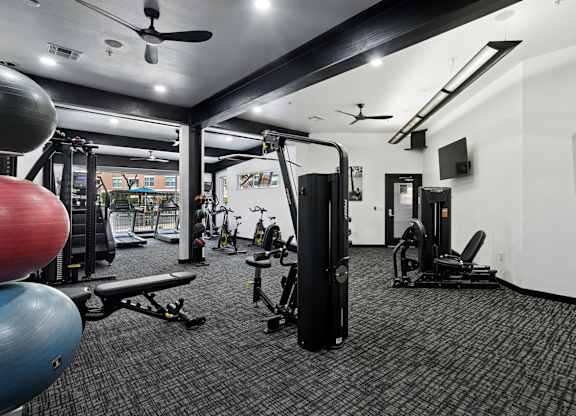 A gym with a variety of equipment including a weight machine, a bench, and a fan.