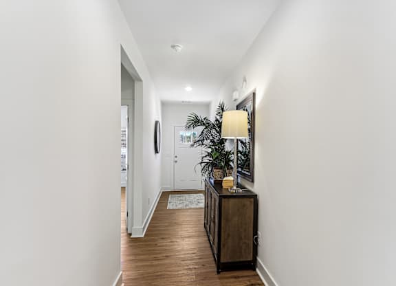 a hallway with white walls and a wooden floor and a table with a lamp