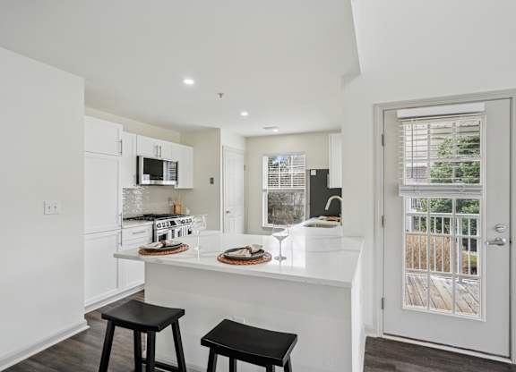 A kitchen with white cabinets and a white island with a counter top and two black stools.