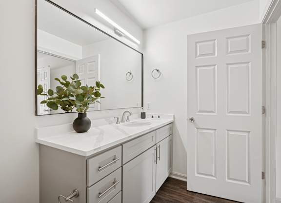 A bathroom with a white door and a mirror above a sink.