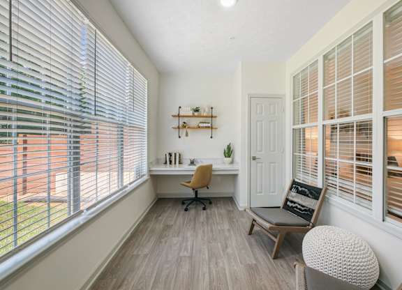 A room with a desk, chair, and window blinds.