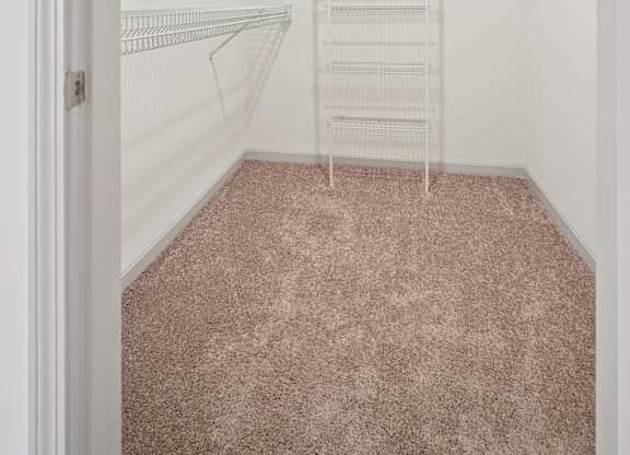 A walk-in closet with white shelving and a pink carpet.