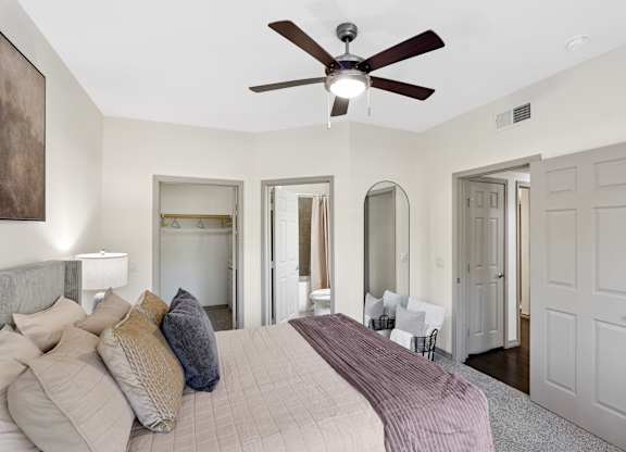 A bedroom with a bed, a ceiling fan, and a mirror.