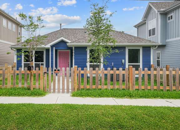 A blue house with a red door and a wooden fence in front.