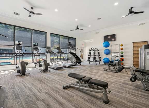 A spacious home gym with a variety of exercise equipment and a view of a pool outside the windows.
