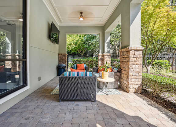 A patio with a wicker sofa and a table with a yellow vase on it.