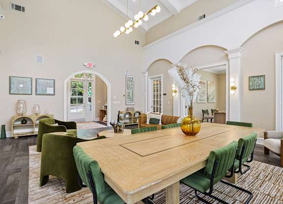 A large wooden table with green chairs is in the center of a spacious room.