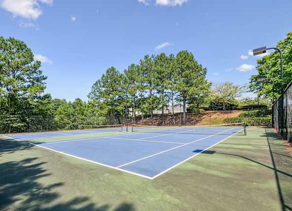 A tennis court surrounded by trees and a fence.