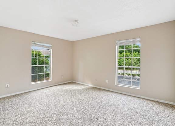 A room with carpeted floor and two windows.