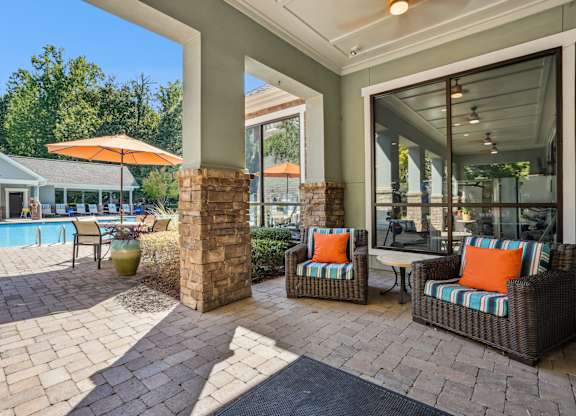 A patio with a pool and a chair with an orange pillow.