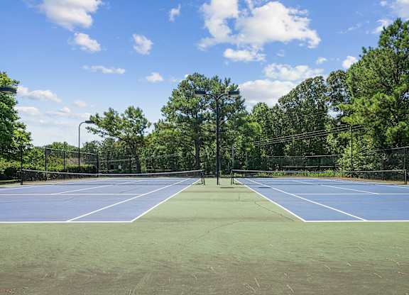 A tennis court surrounded by trees and a fence.