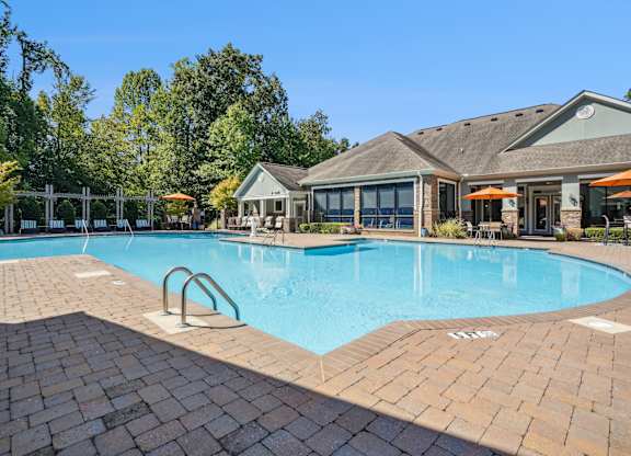 A large outdoor swimming pool surrounded by a brick patio and a small building.