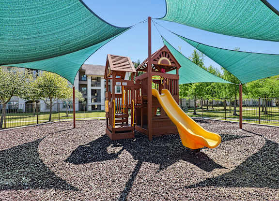 Shaded playground with a yellow slide and a green canopy.