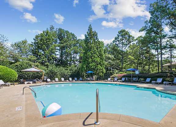 A pool surrounded by trees and chairs.