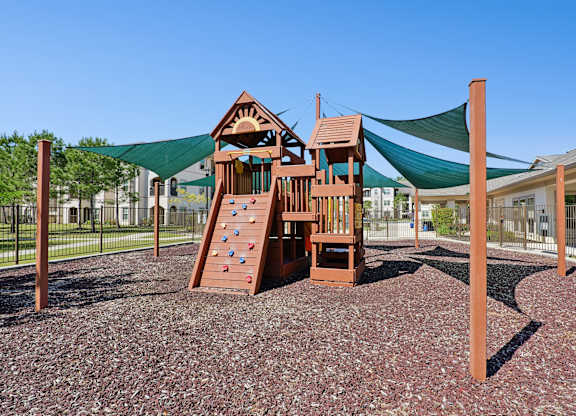 A playground with a wooden structure and a green shade sail.
