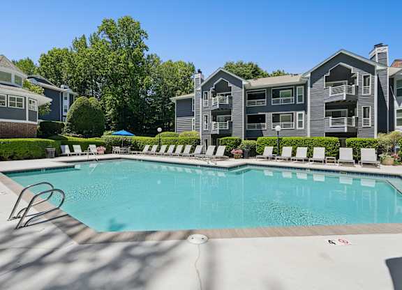 A swimming pool surrounded by lounge chairs in front of apartment buildings.