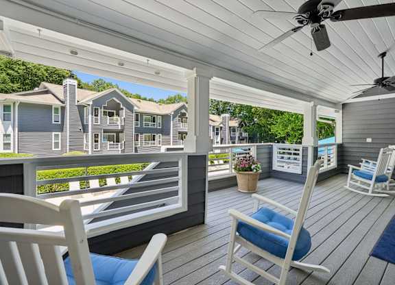 A white porch with a ceiling fan and two chairs.