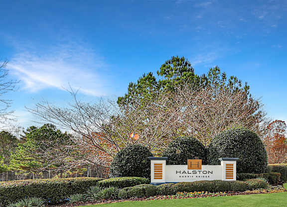 A sign that says Halston in front of a green lawn.