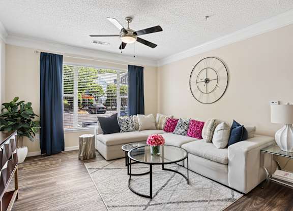 A living room with a white couch, a glass table, and a ceiling fan.