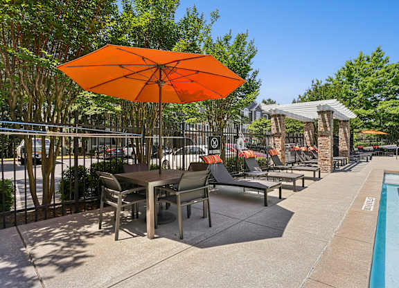 A large orange umbrella is in the foreground of a poolside area.