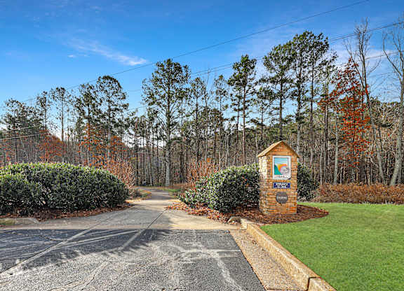 A sign in front of a hedge surrounded by trees.