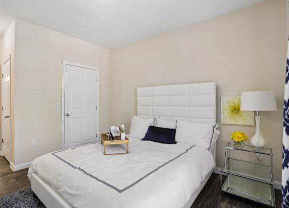 A bedroom with a white bed and a nightstand with a lamp.