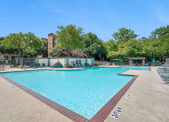 A large swimming pool surrounded by trees and a building in the background.