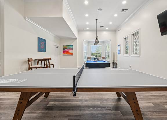 A ping pong table is in the middle of a room with a white wall and a window.